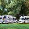 Three white motorhomes parked next to each other in a grassy campsite.