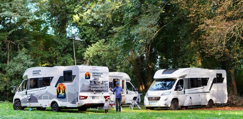 Three white motorhomes parked next to each other in a grassy campsite.